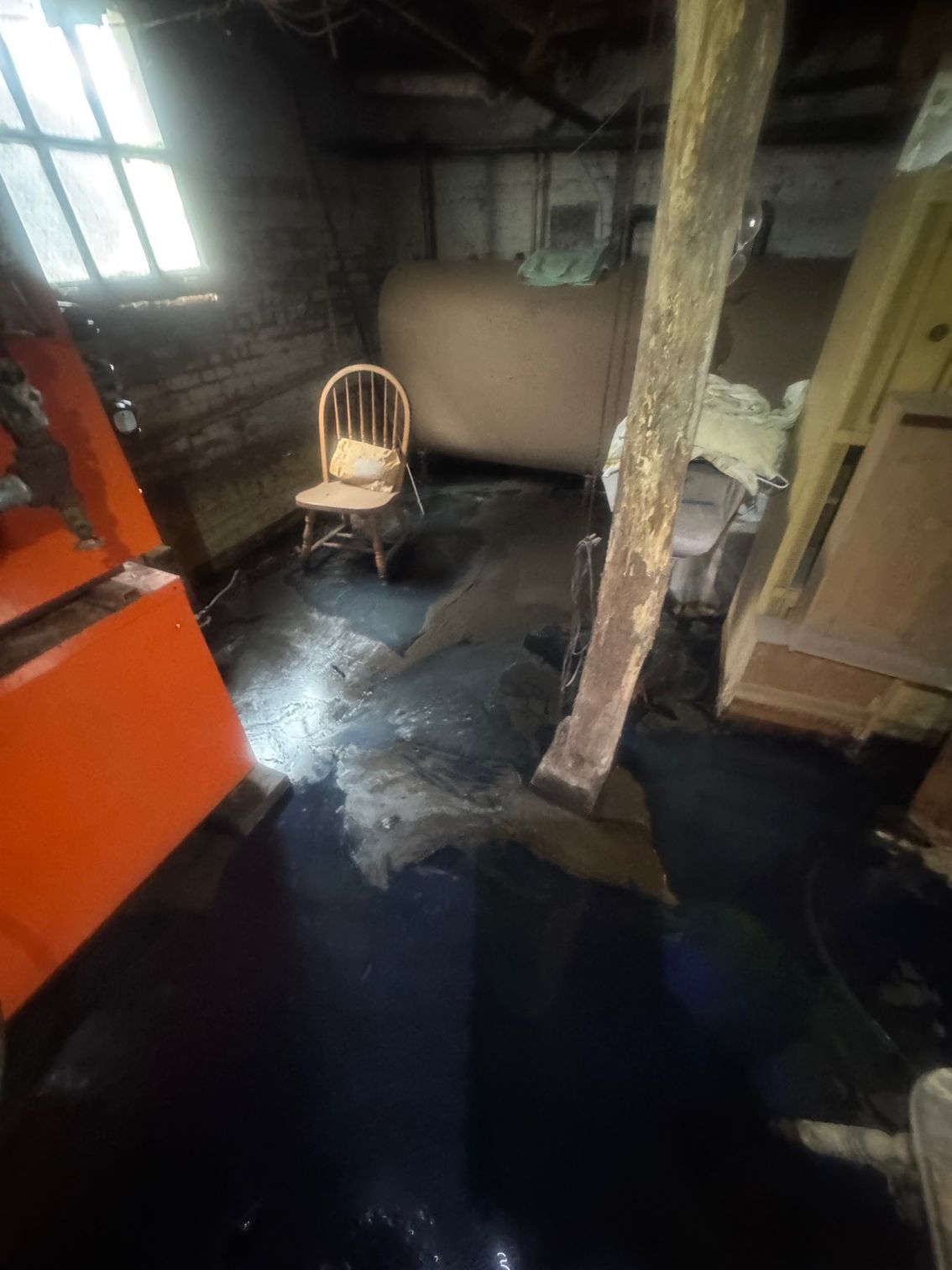 Dark, flooded basement with a chair, oil tank, and wooden supports.
