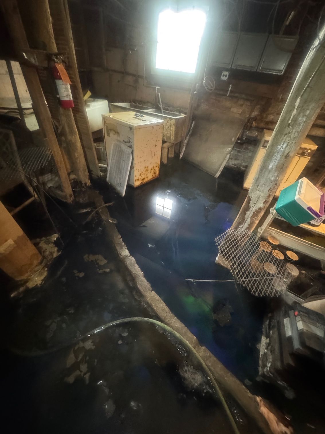 Flooded basement with standing water, appliances, and dim lighting.