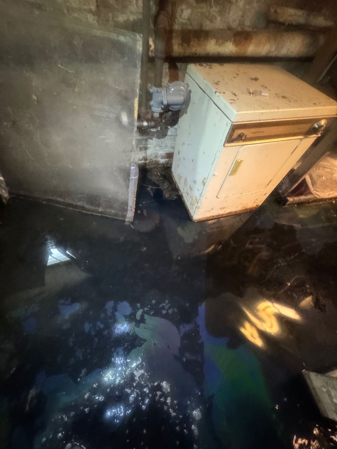 Flooded basement with standing water.  Appliances and walls are partially submerged.  Oil slick on water's surface.