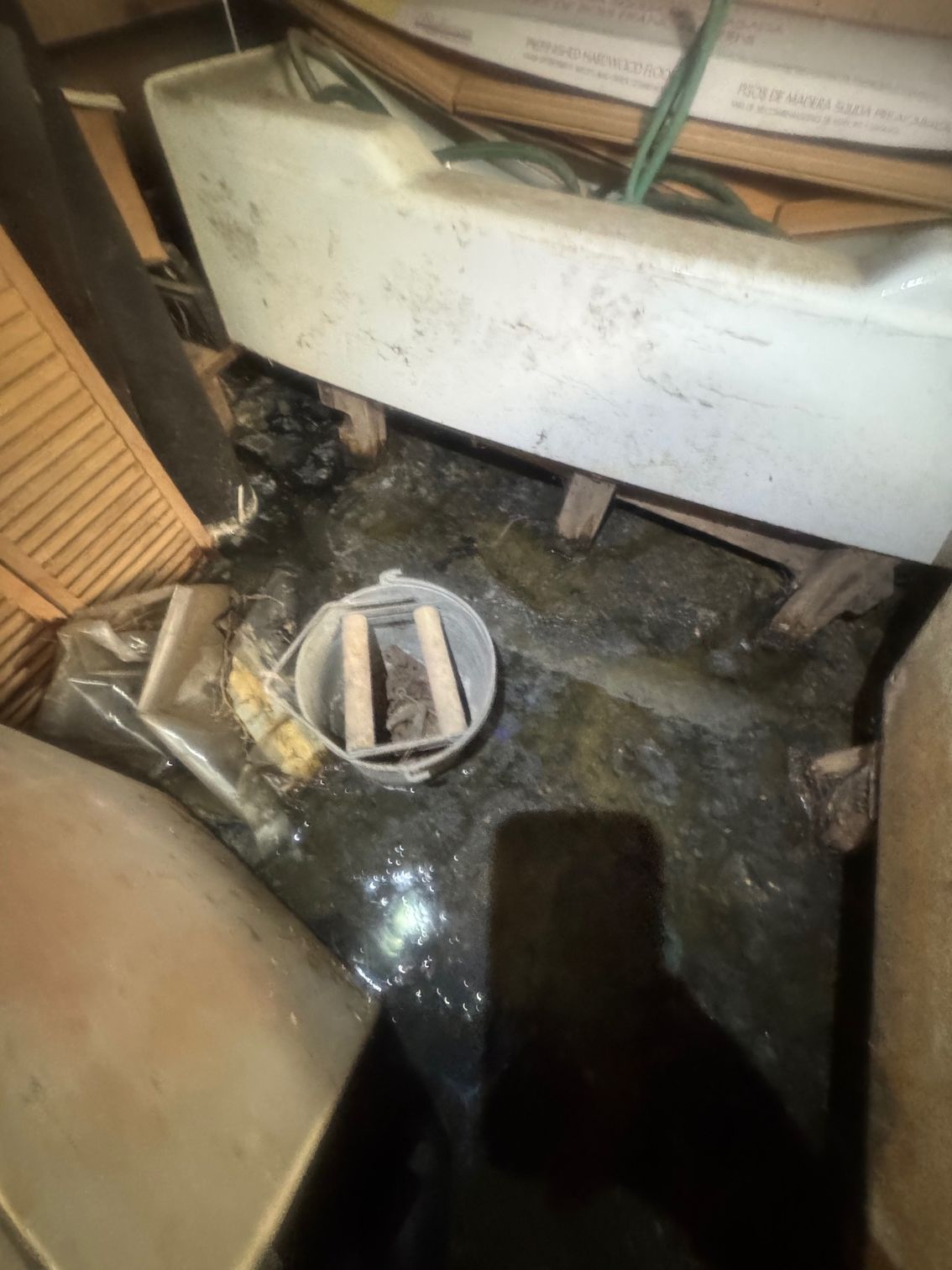 Flooded storage area with debris, a bucket, and boat parts. Dark, wet environment.