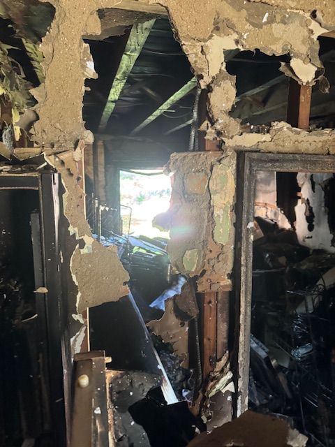 Interior view of fire-damaged building with exposed beams, rubble, and view to outside.