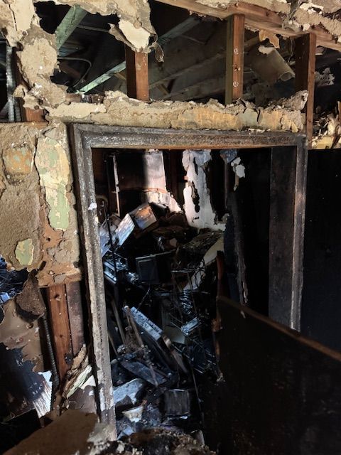 Interior room heavily damaged by fire; charred debris, collapsed ceiling, blackened walls.