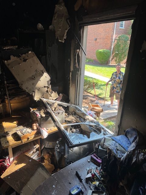 Interior view of a damaged room, debris scattered, doorway open to a person outside.