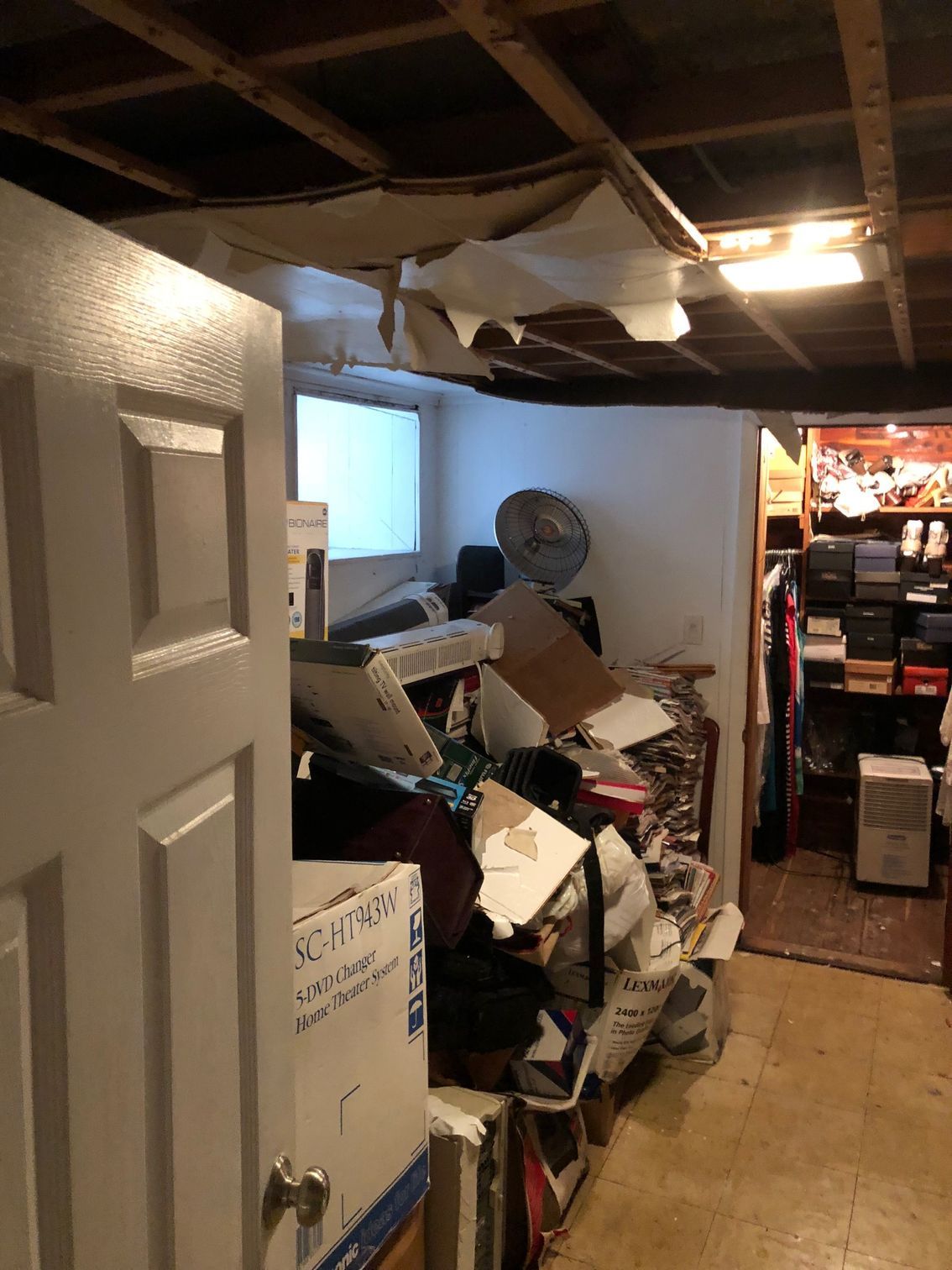 Cluttered storage room with boxes, debris, exposed ceiling, and a doorway to a closet.