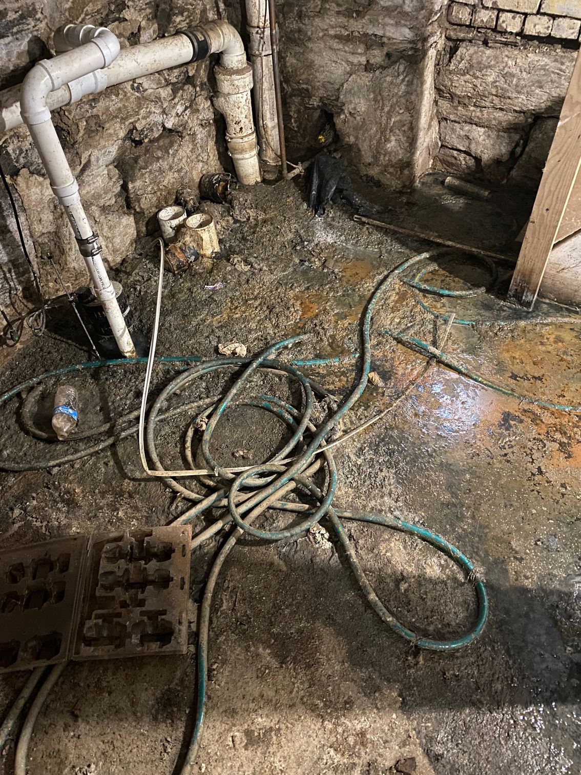 Messy basement with pipes, hoses, and water on the floor.