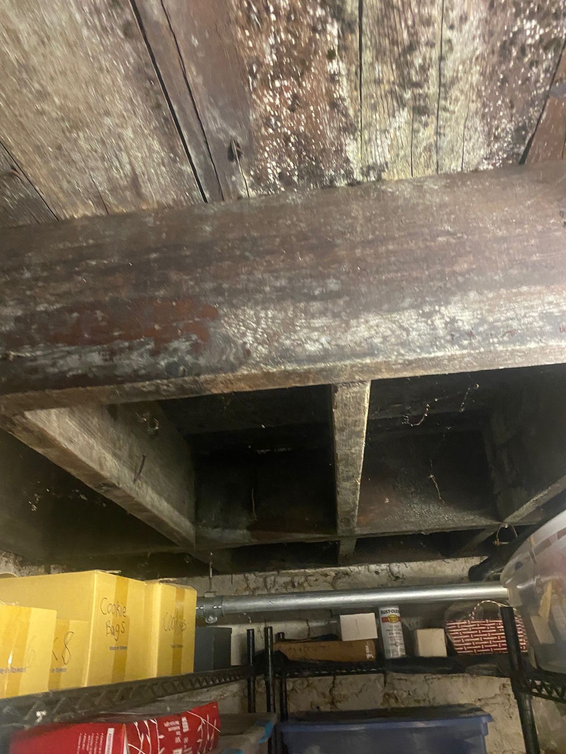 Wooden ceiling with beams, showing discoloration and possible mold. Below are shelves and containers.
