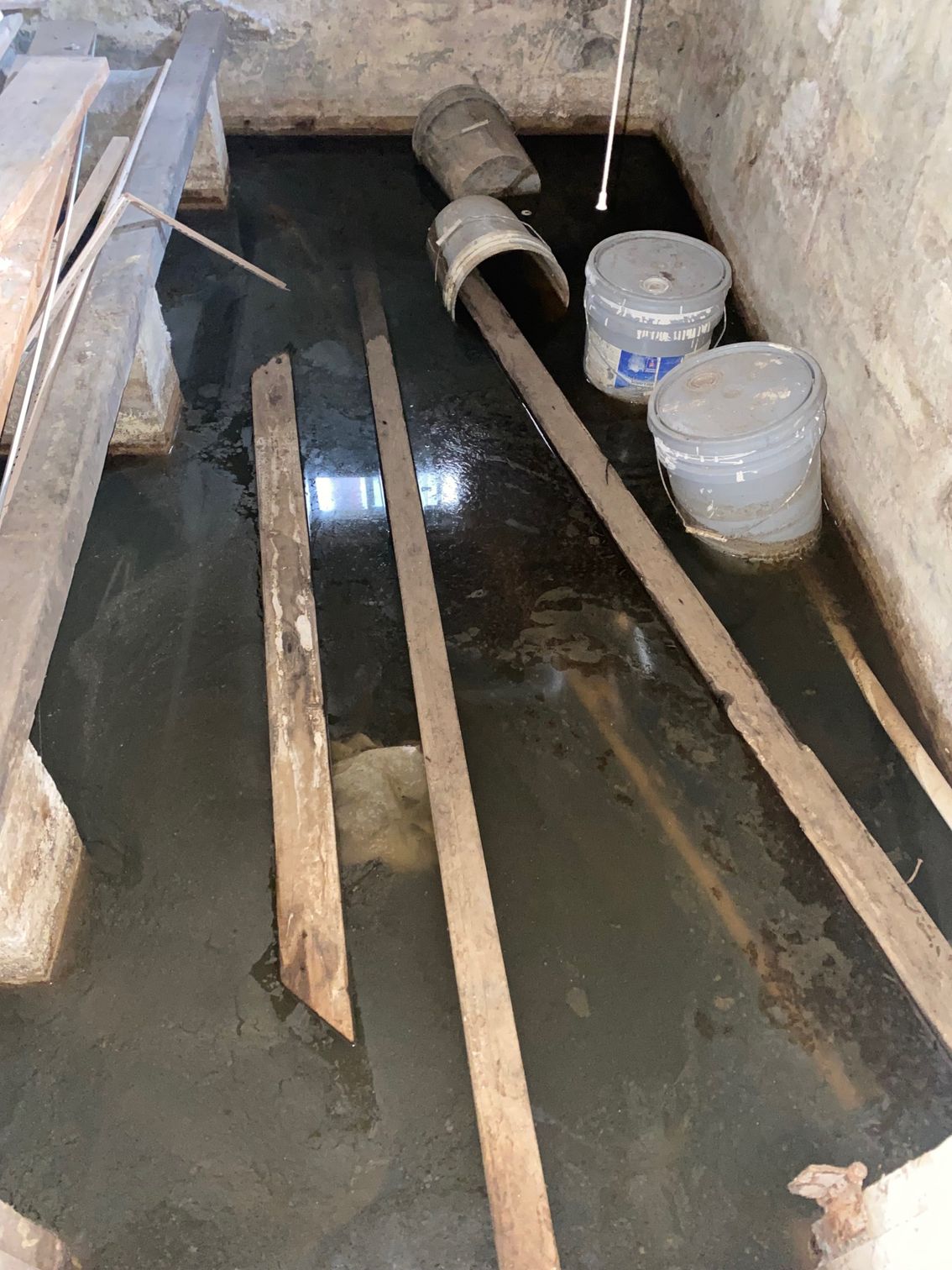 Flooded basement with wooden beams and buckets; water covers the floor.