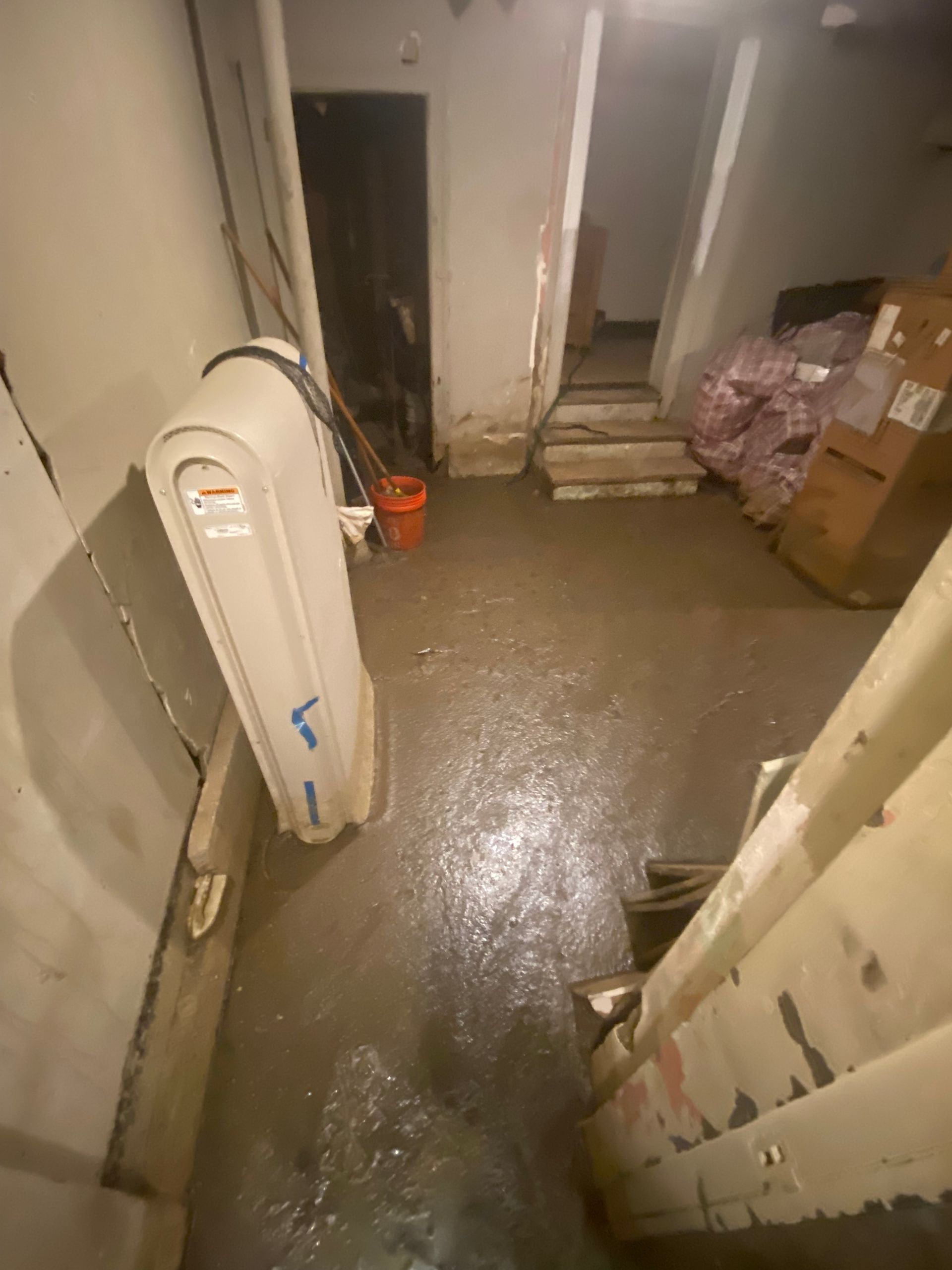 Flooded basement with standing water, a dehumidifier, and stairs leading upwards.