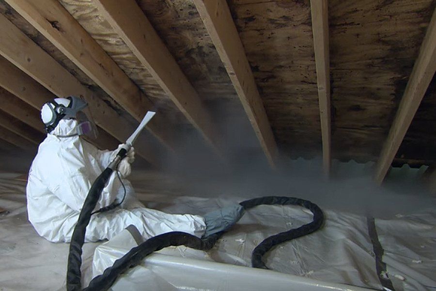 Person in protective suit spraying insulation in an attic.