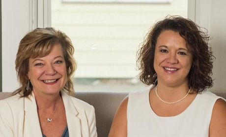 Two women are sitting next to each other on a couch and smiling for the camera.