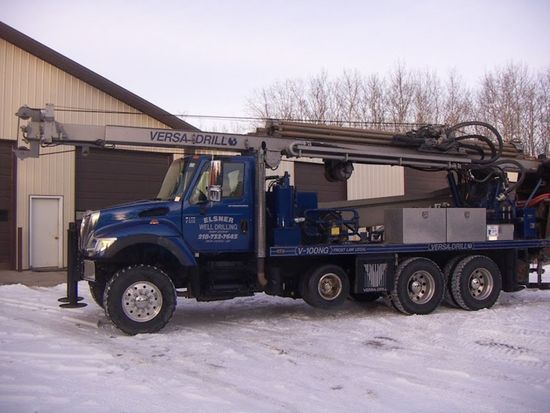 A blue Versa-Drill truck parked on a snowy lot in front of a metal building.