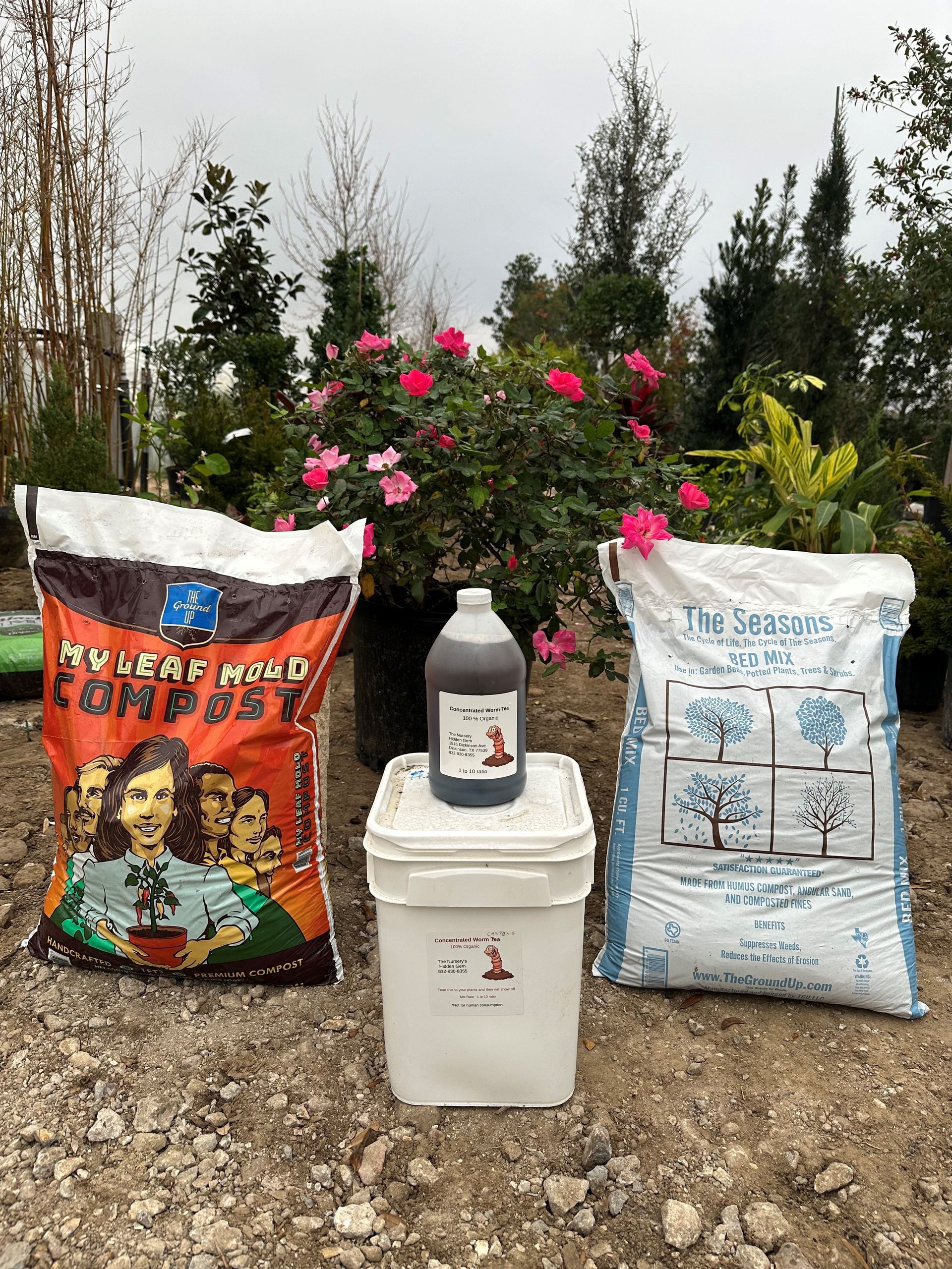 A bucket , a bag of compost , and a bottle of liquid are sitting next to each other on the ground.