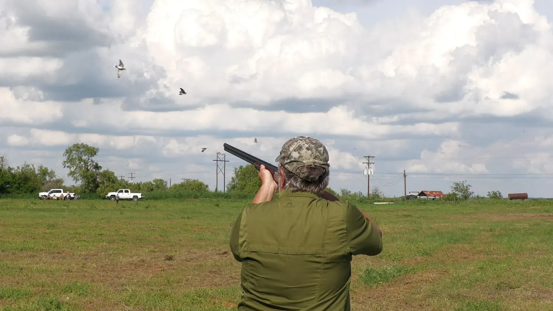 Man shooting a rifle in an open green field.