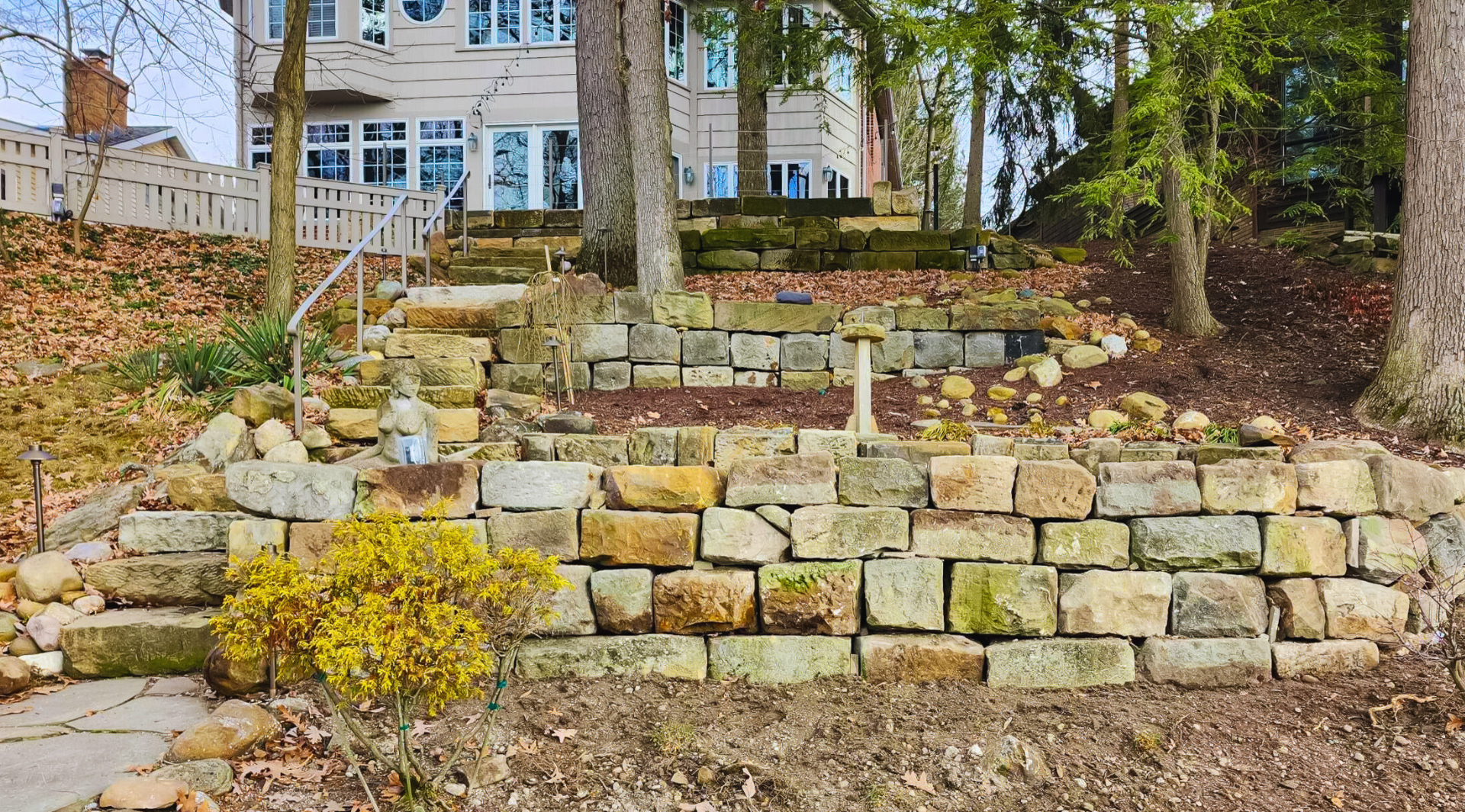 A stone wall in a yard with a house in the background.