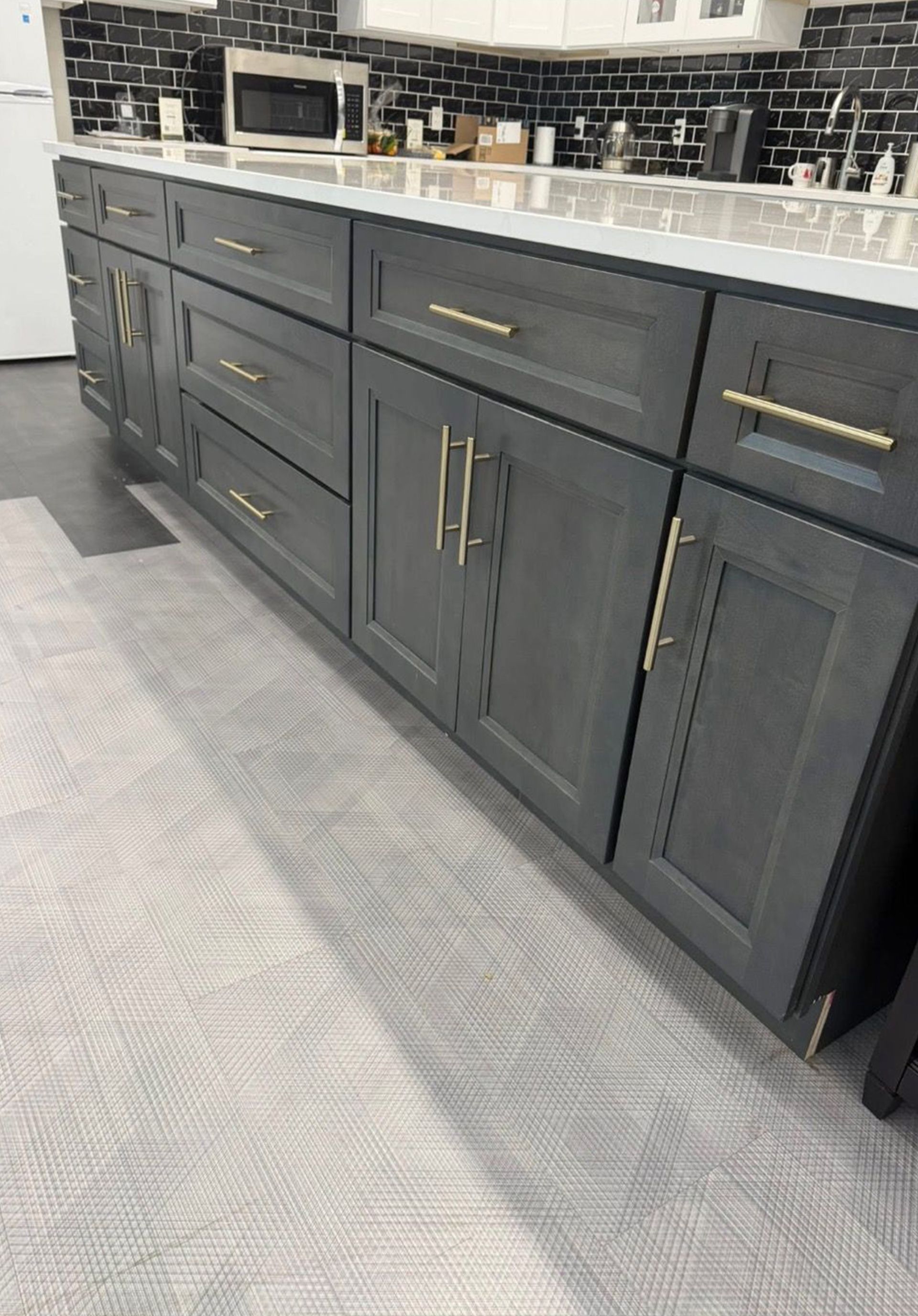 Dark gray kitchen cabinets with gold handles and a black tile backsplash in a modern kitchen