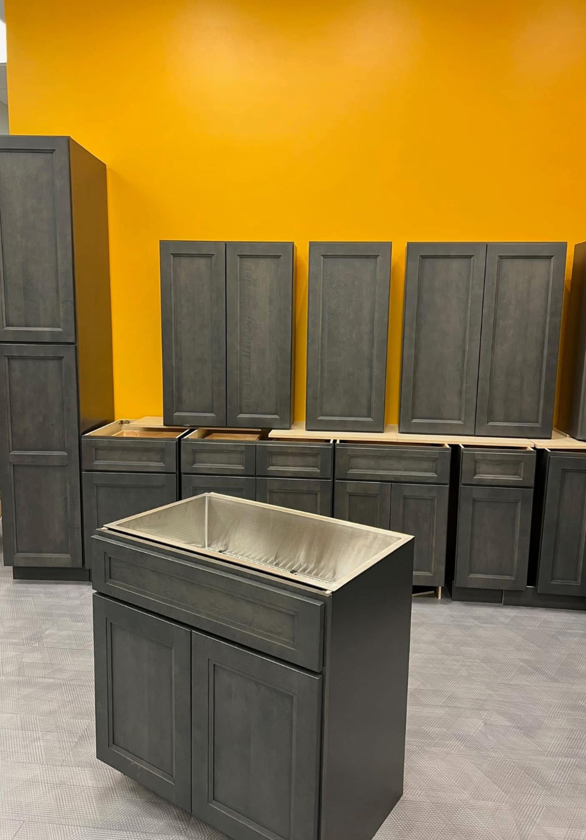 Dark kitchen cabinets and a sink island against a bright yellow wall in a showroom.