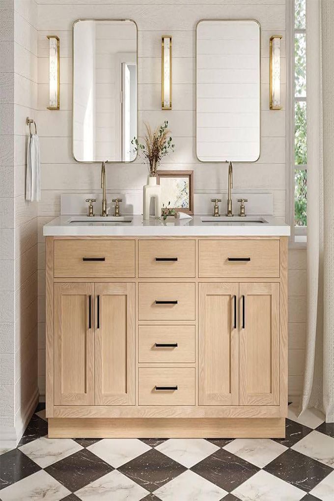 Light wood bathroom vanity with double sinks, mirrors, wall sconces, and black-and-white floor tiles.