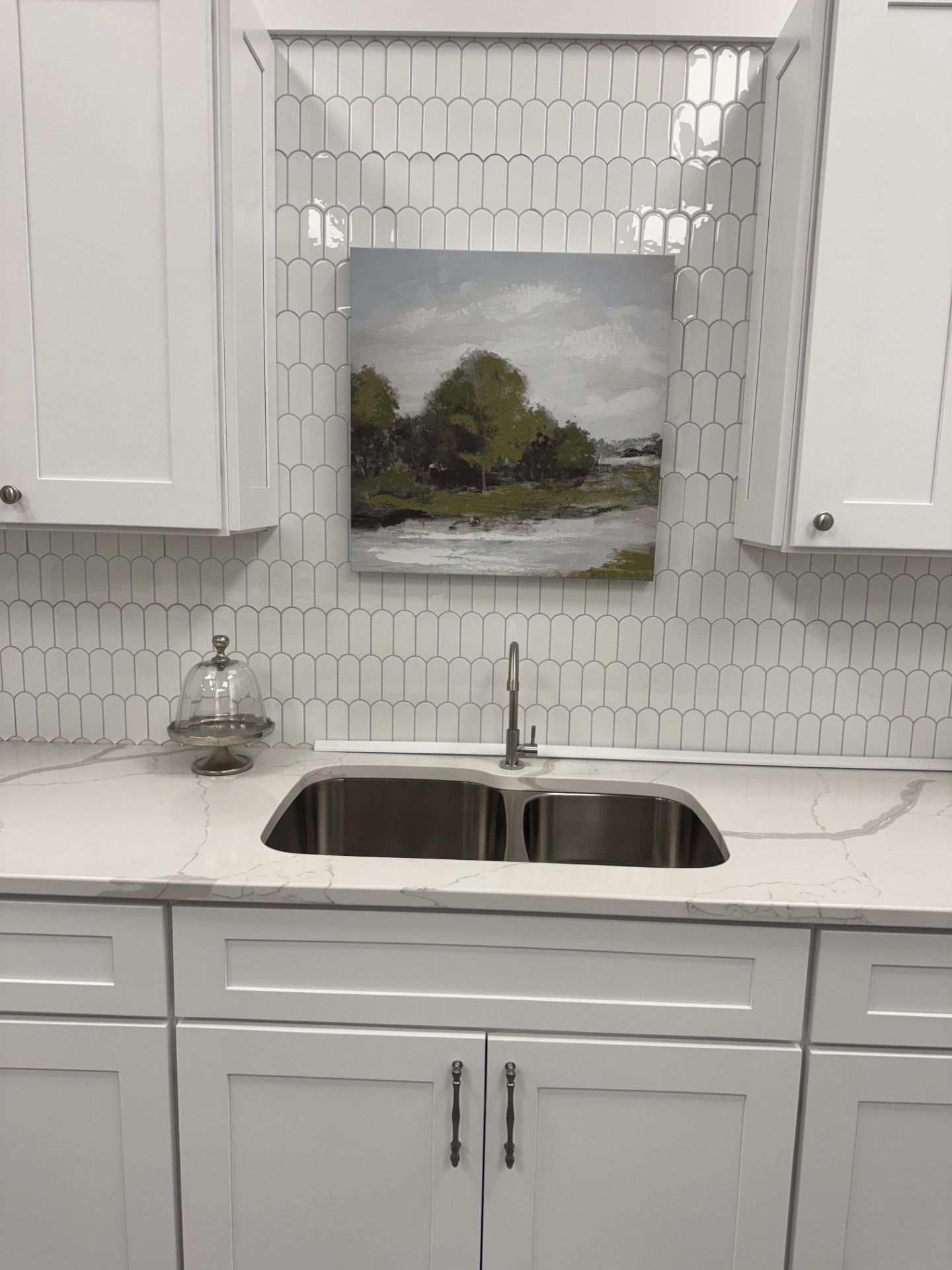 Bright white kitchen with subway tile, farmhouse sink, and landscape painting above the faucet
