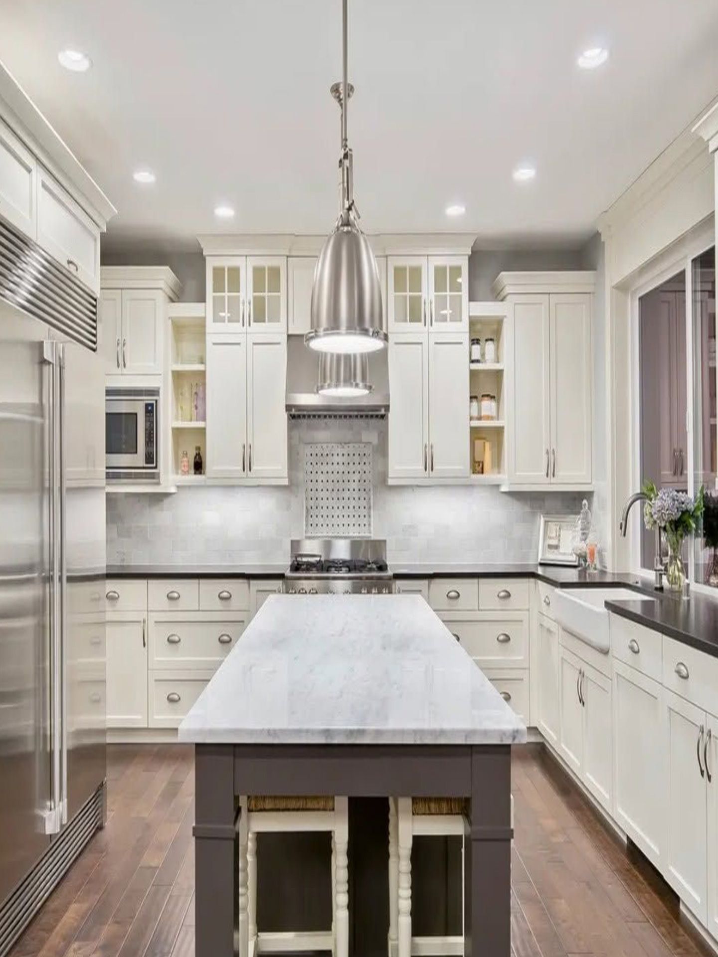 Bright white modern kitchen with marble island, stainless range hood, and recessed ceiling lights