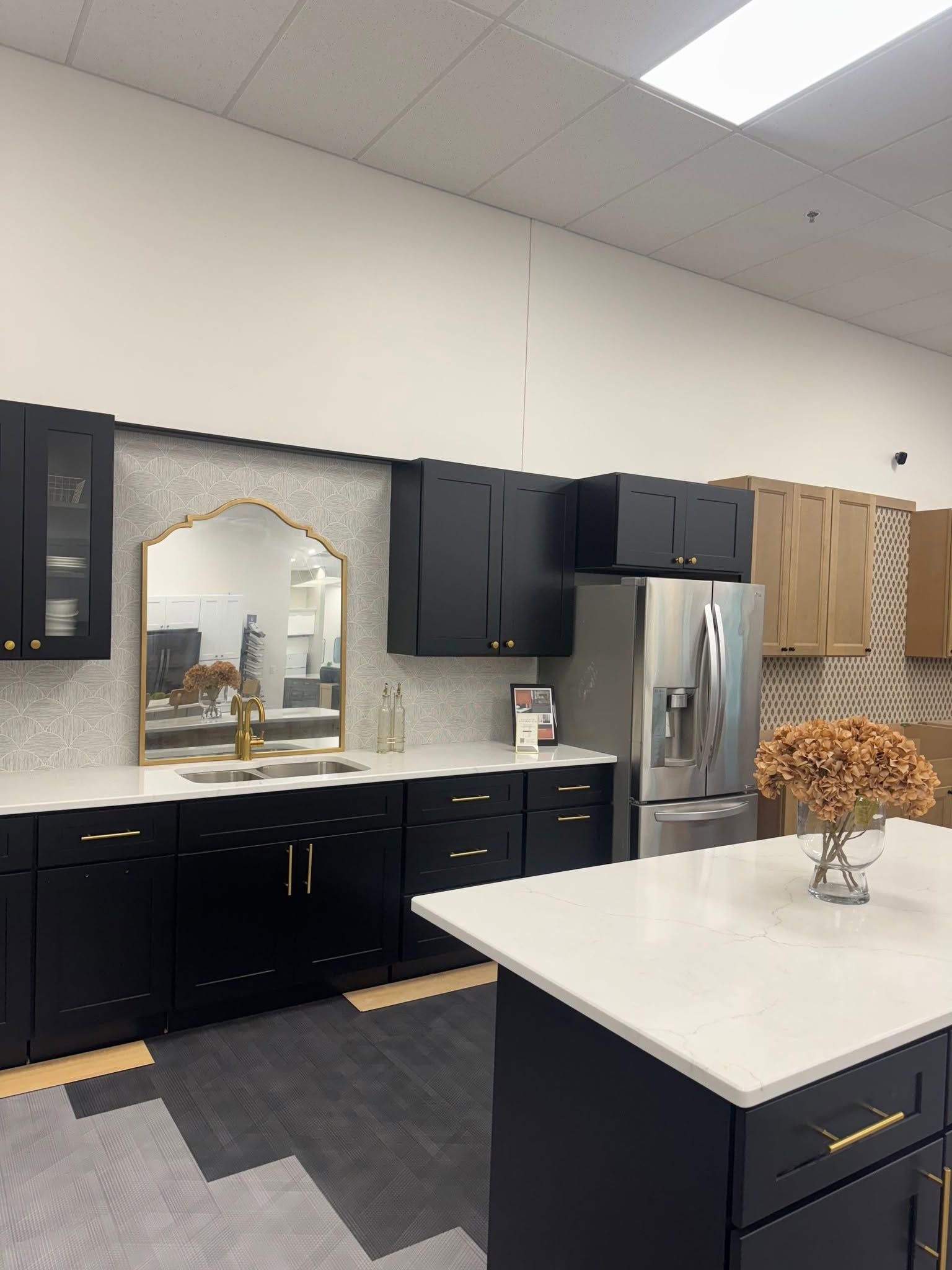Modern kitchen with black cabinets, stainless fridge, white island, and a decorative mirror above the sink.