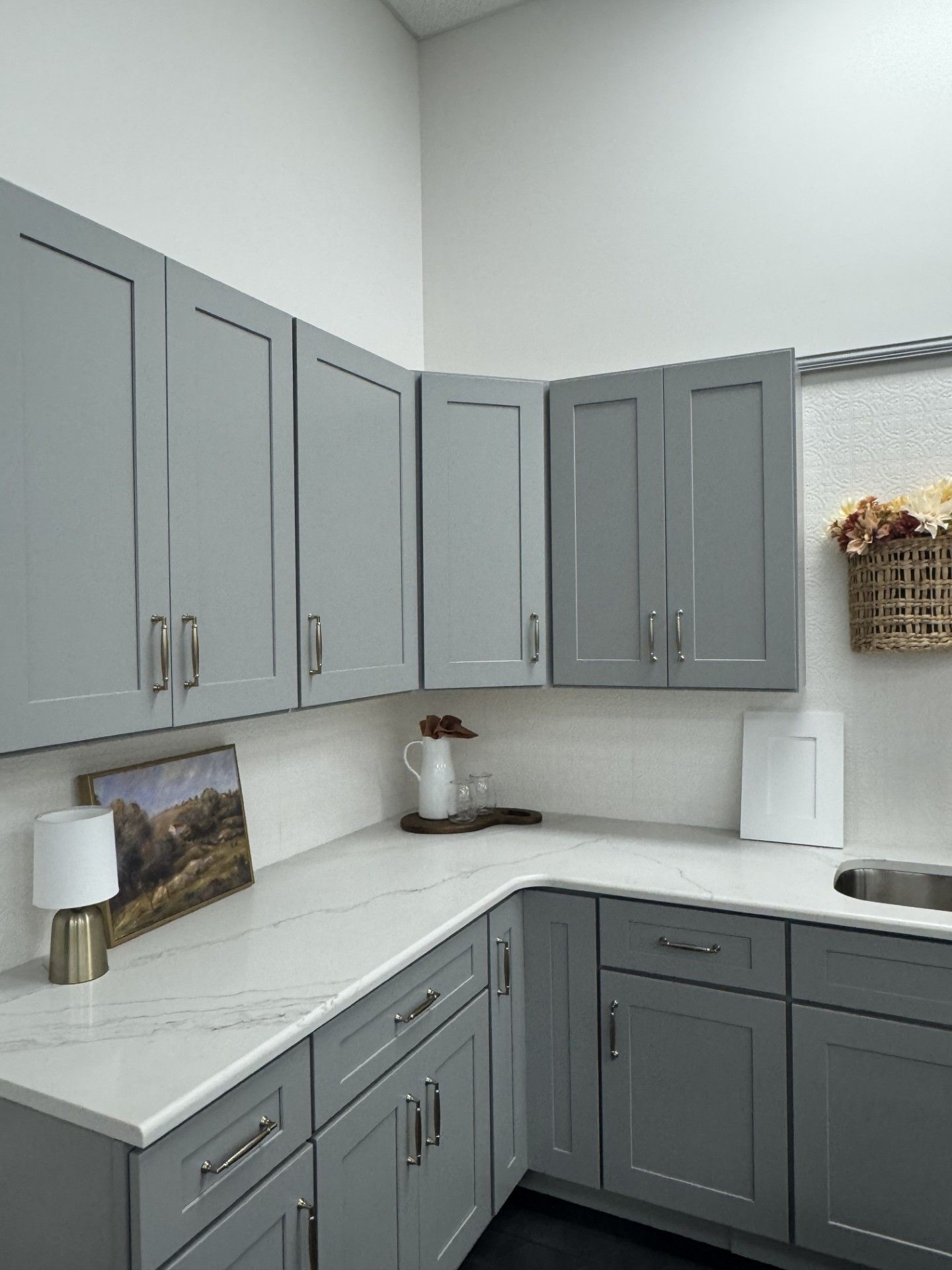 Gray kitchen with white countertops, dark hardware, and a corner sink beneath upper cabinets