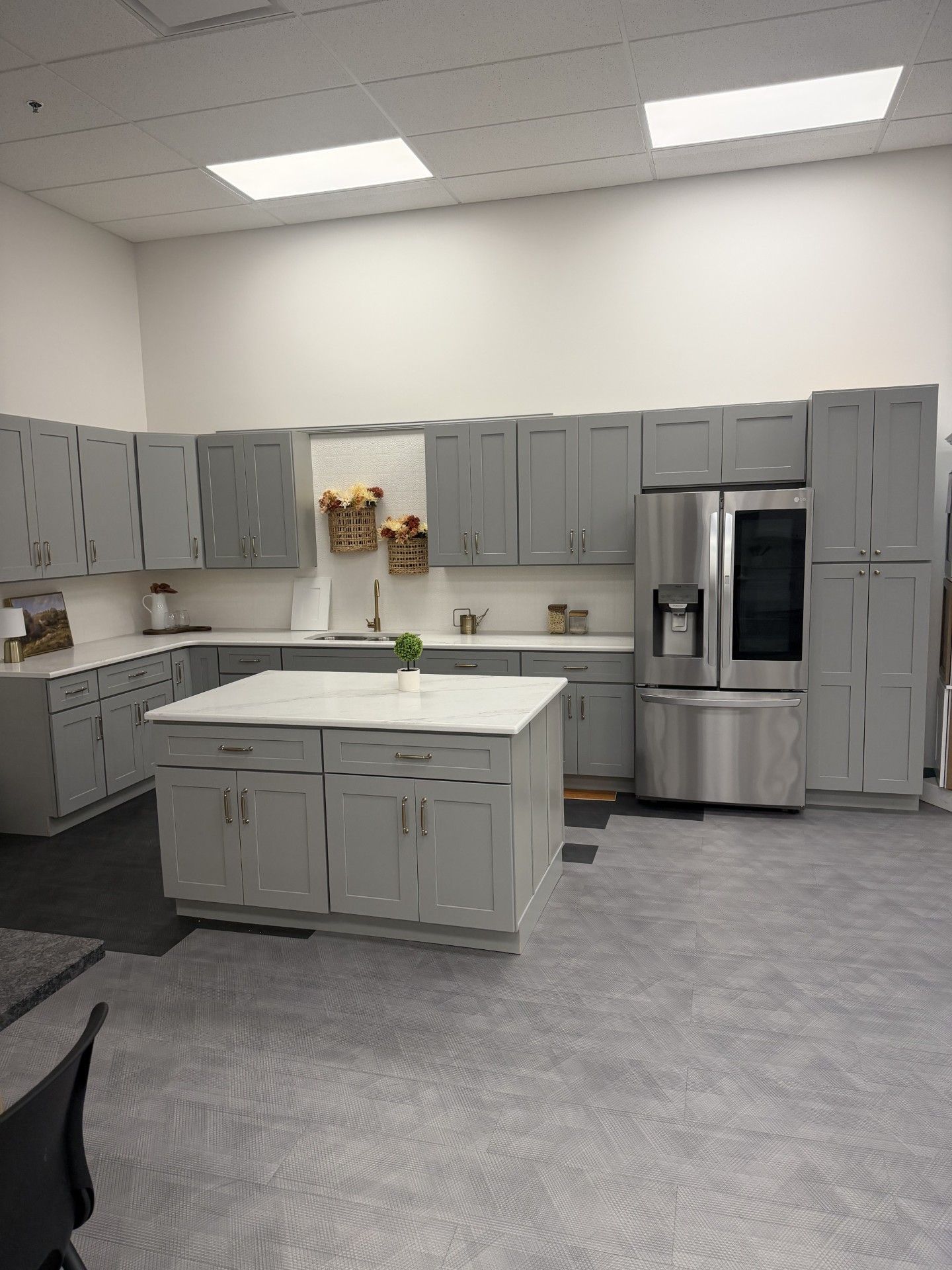 Empty break room kitchen with gray cabinets, island, stainless steel appliances, and fluorescent ceiling lights