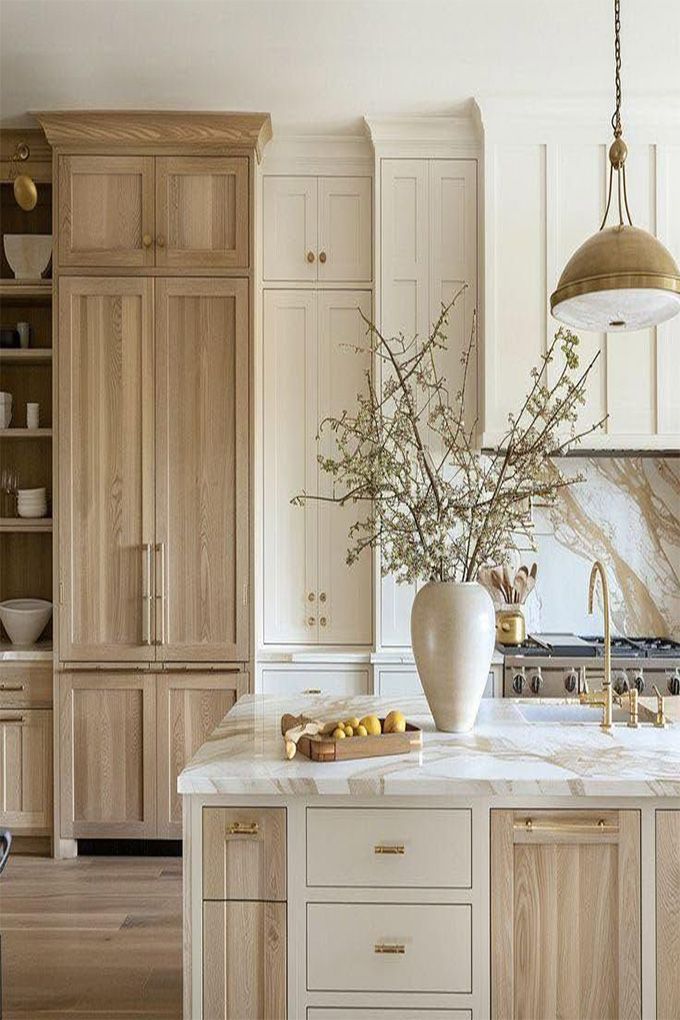 Bright kitchen with white island, marble countertop, vase of branches, and tall wood cabinets
