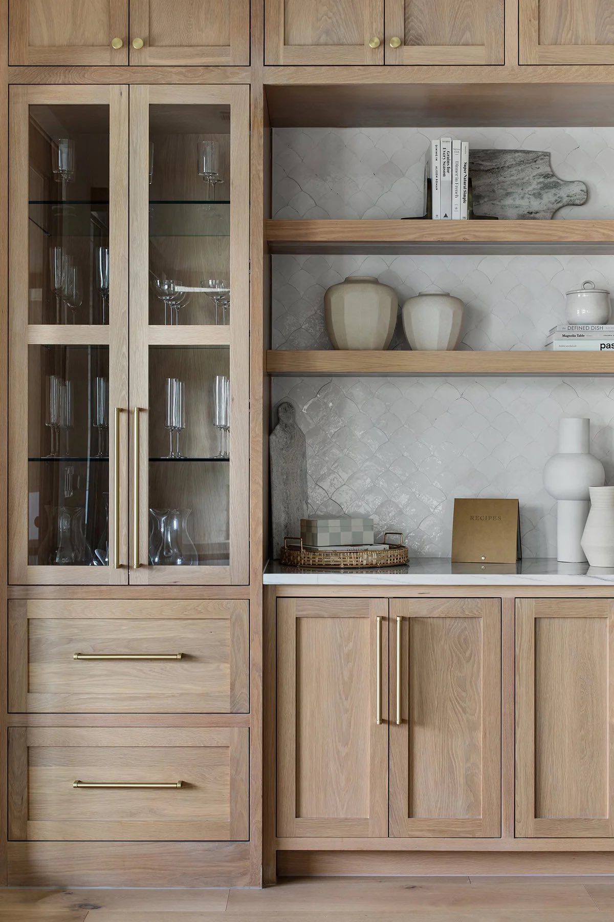 Built-in wooden cabinet with glass doors, shelves, and drawers, holding glassware and decorative objects.