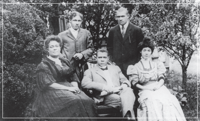 Black-and-white outdoor family portrait with five people seated and standing in a garden.