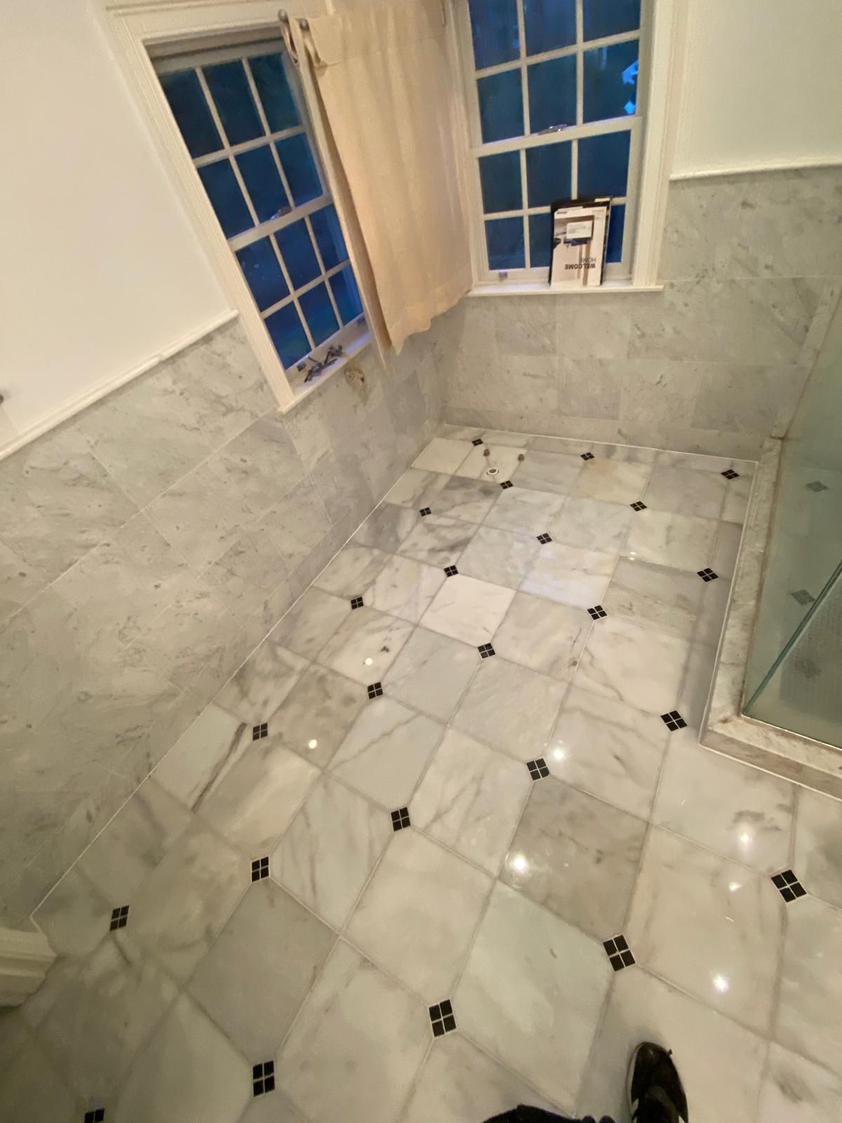 Bathroom with marble floor tiles in a diamond pattern, two windows, and shower.