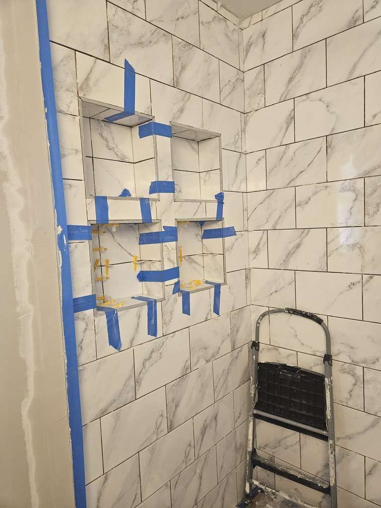 Shower niche with tiled walls, blue tape, and a small ladder.