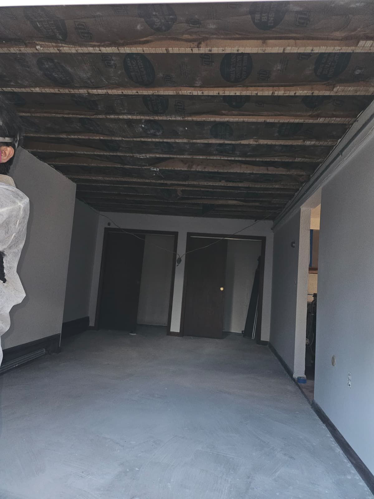 Room with unfinished ceiling, gray walls, two dark doors, and concrete floor.