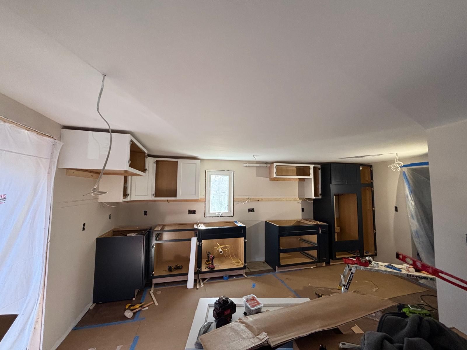 Kitchen renovation: Unfinished cabinets installed on walls, exposed drywall, wires, and tools visible.