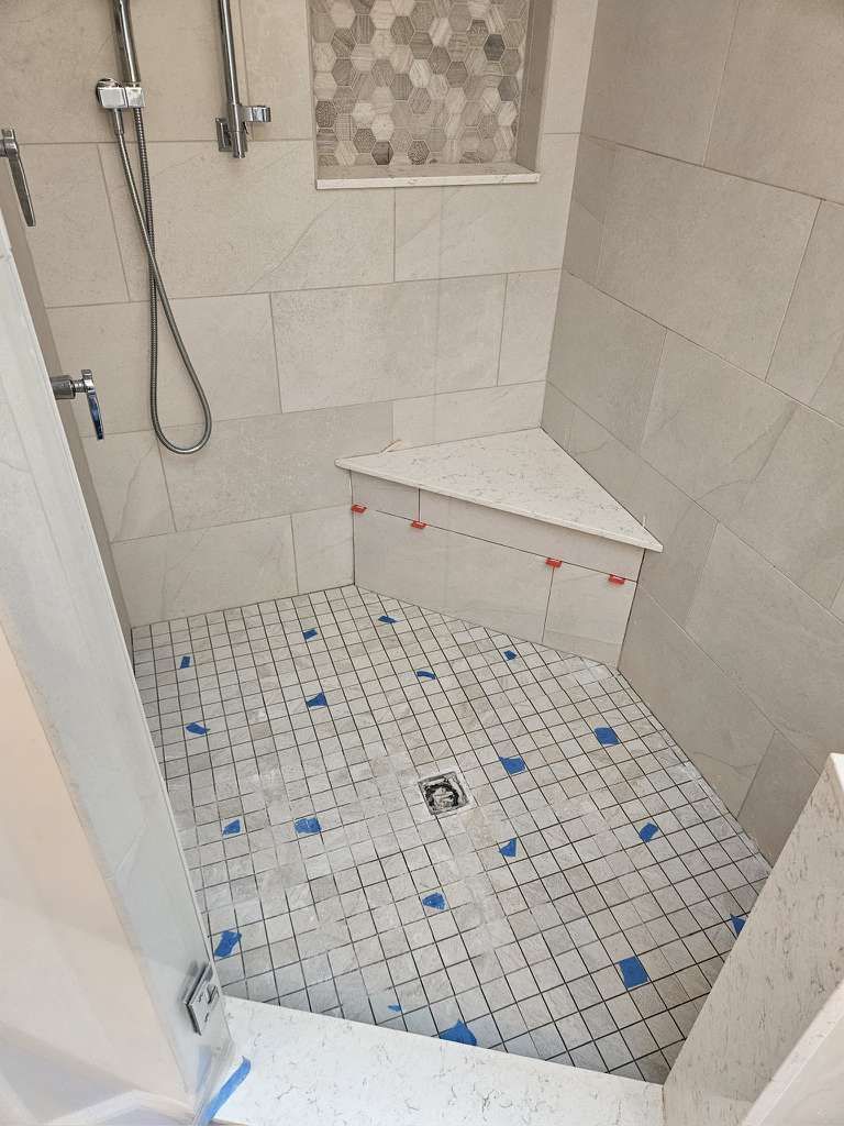 Shower stall with white tile walls and floor, hexagon tile niche, corner seat, and shower fixtures.