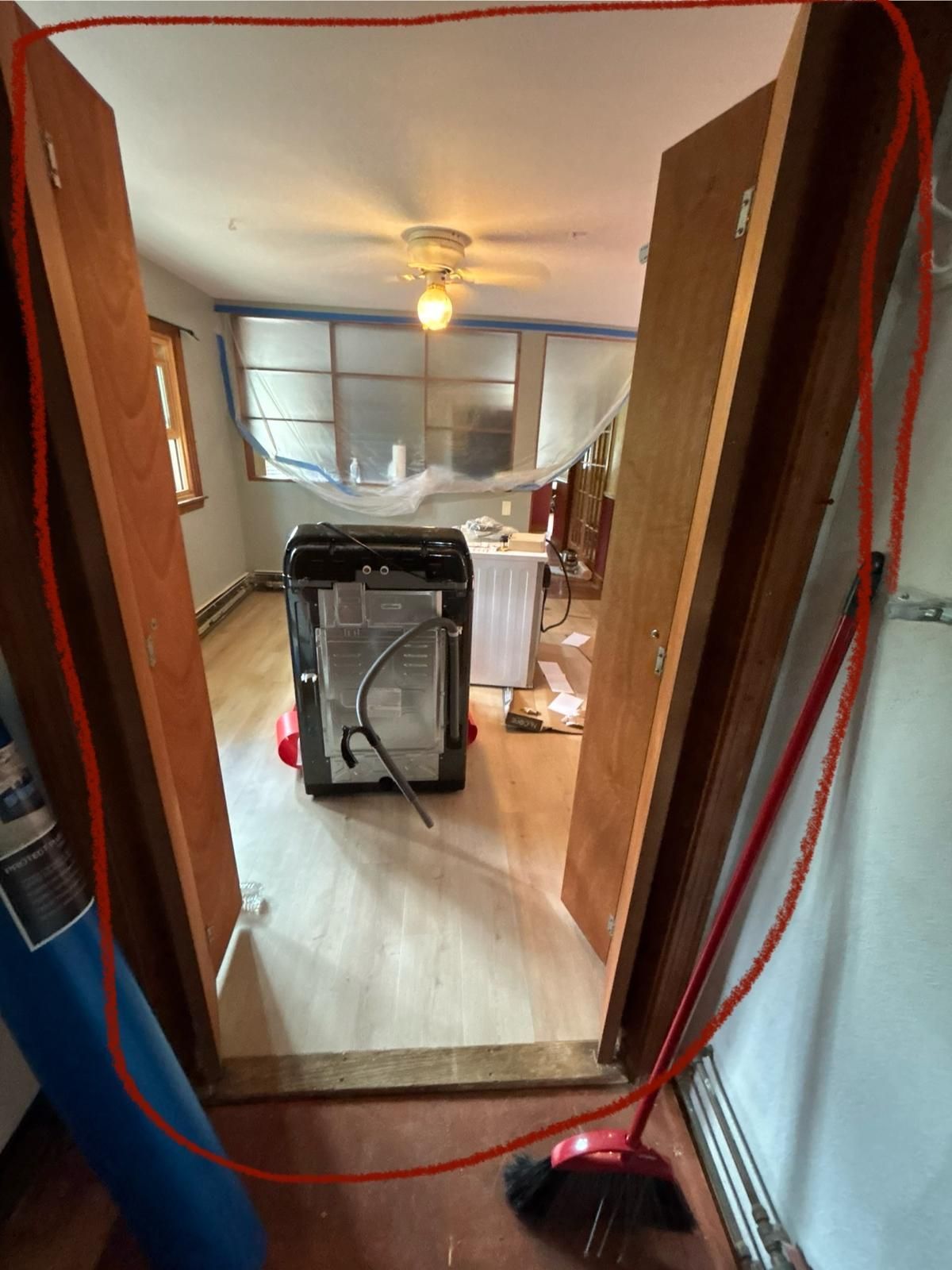 Doorway with two wooden doors open. Room has appliance, exposed framing, and red trim.