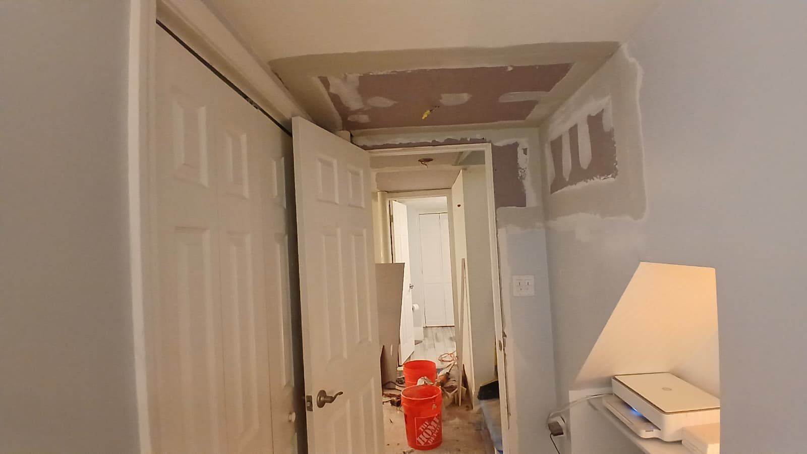 Hallway under construction with damaged ceiling and open doors. A bucket sits on the floor.
