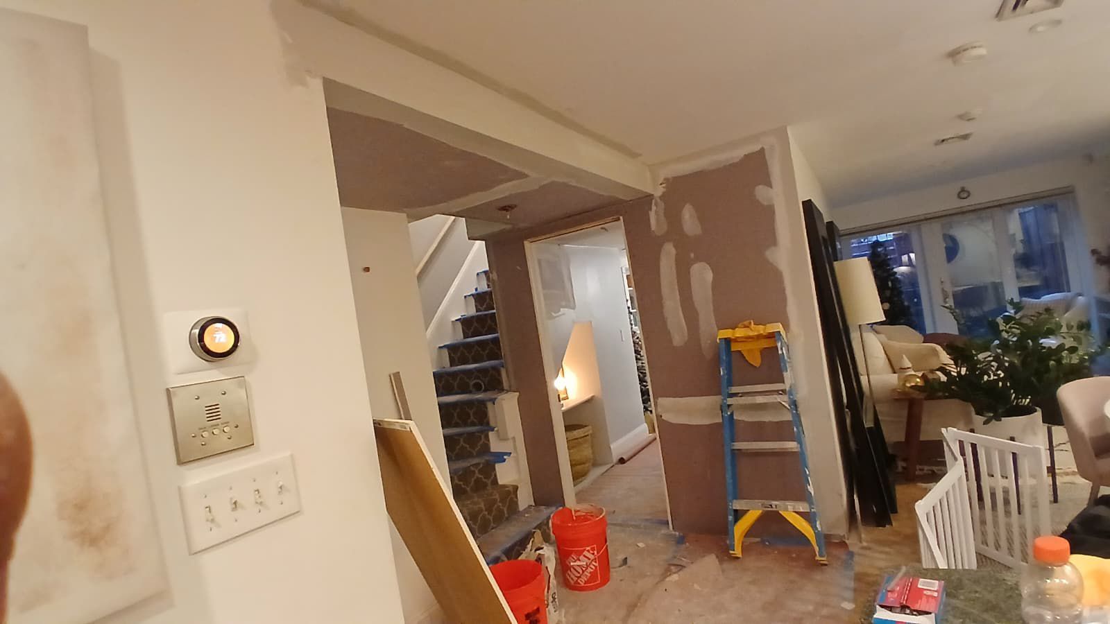 Interior view of a home renovation in progress with exposed drywall, a ladder, and stairs.