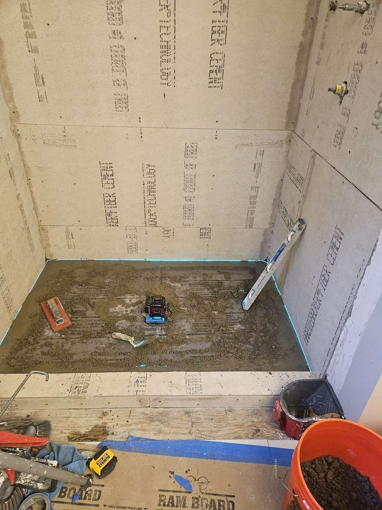 Shower under construction; cement board walls and floor. Tools and bucket visible, including level and saw.