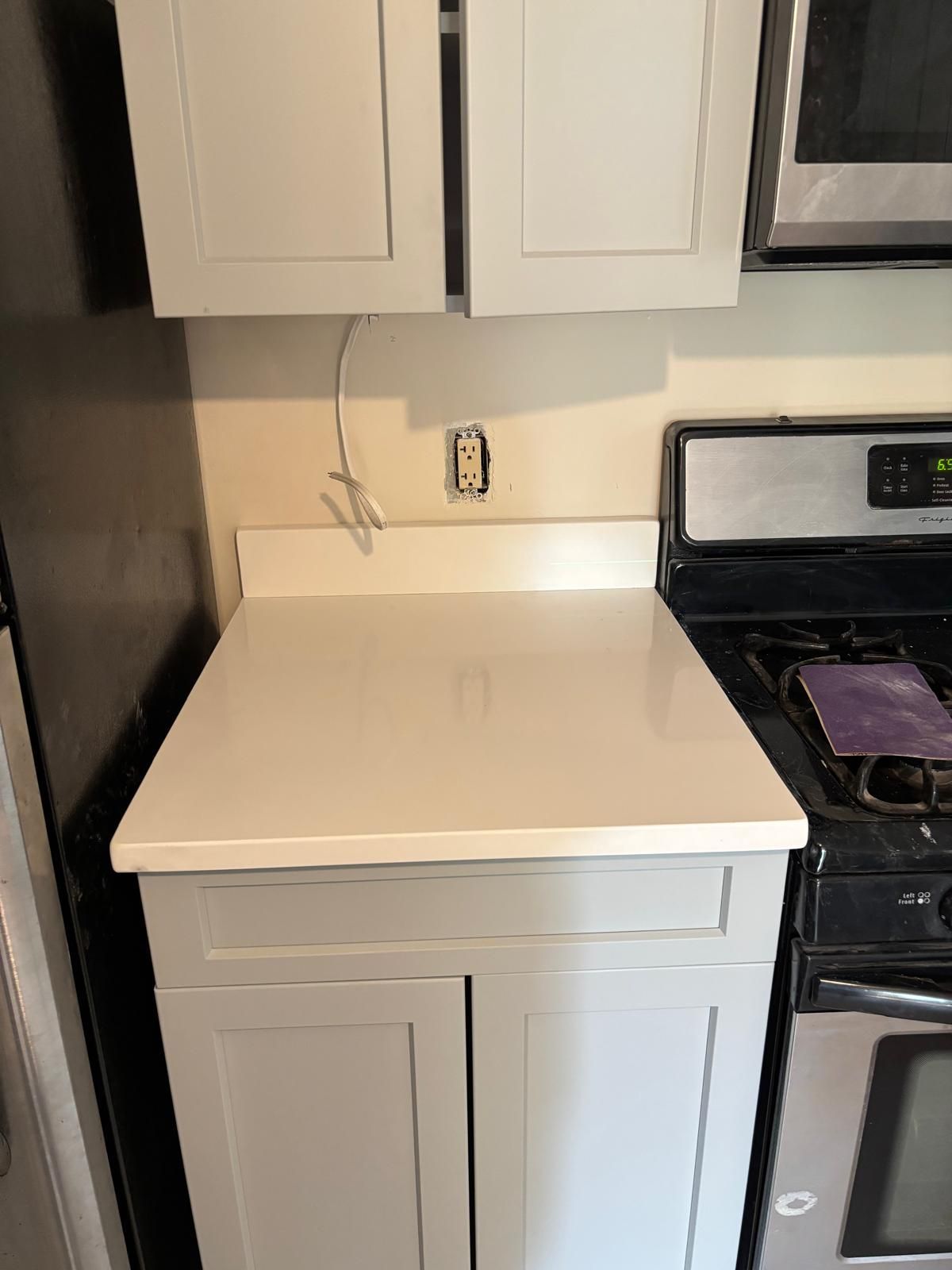Light gray kitchen cabinet with white countertop next to a black and stainless steel stove.