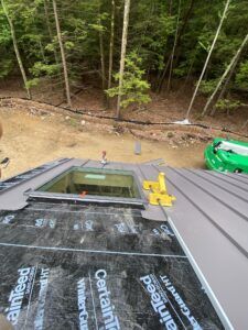A roof with a skylight being installed. The scene is outdoors with trees in the background.