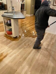 Person mopping wet hardwood floor in a kitchen, water puddles visible. Island and cabinets are in the background.