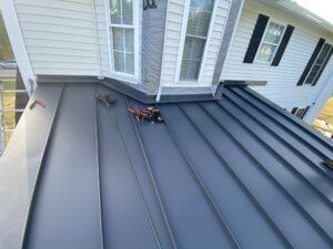 Dark metal roof installation on a house with white siding and black shutters.