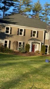 Two-story house with green roof and shutters, beige siding, and red door, set on a green lawn.
