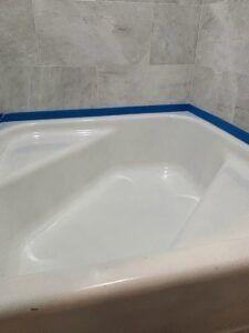 White bathtub with blue tape around the edge against gray tiled wall.