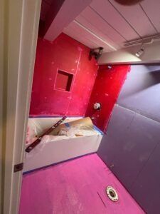 Bathroom under construction with pink and red waterproofing. Tub and plumbing visible.