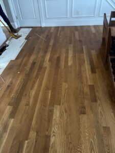 Hardwood floor installation in progress, light brown planks being laid in a room.