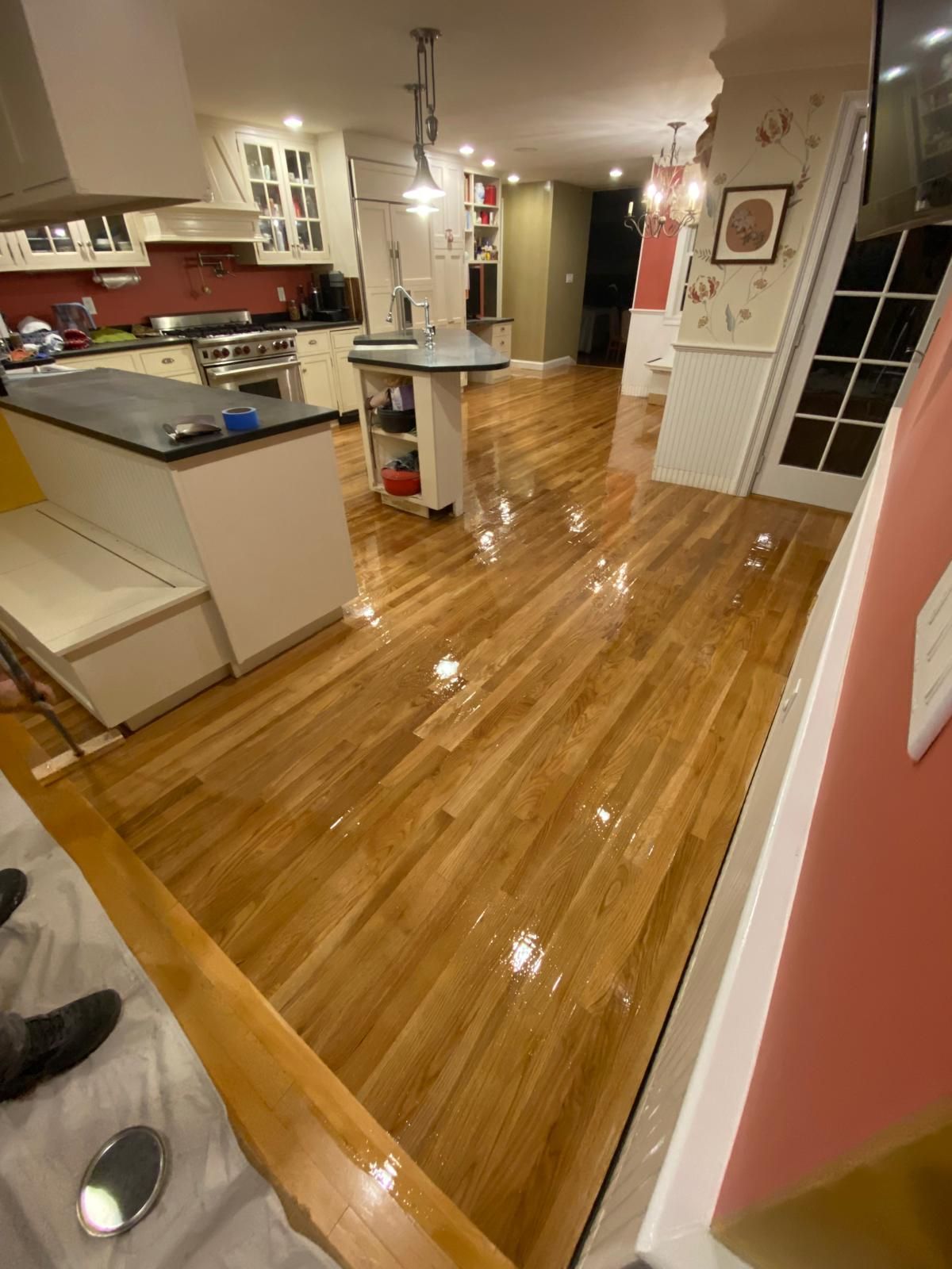 Shiny wooden floors in a kitchen, with cabinets, island, and dining area visible.