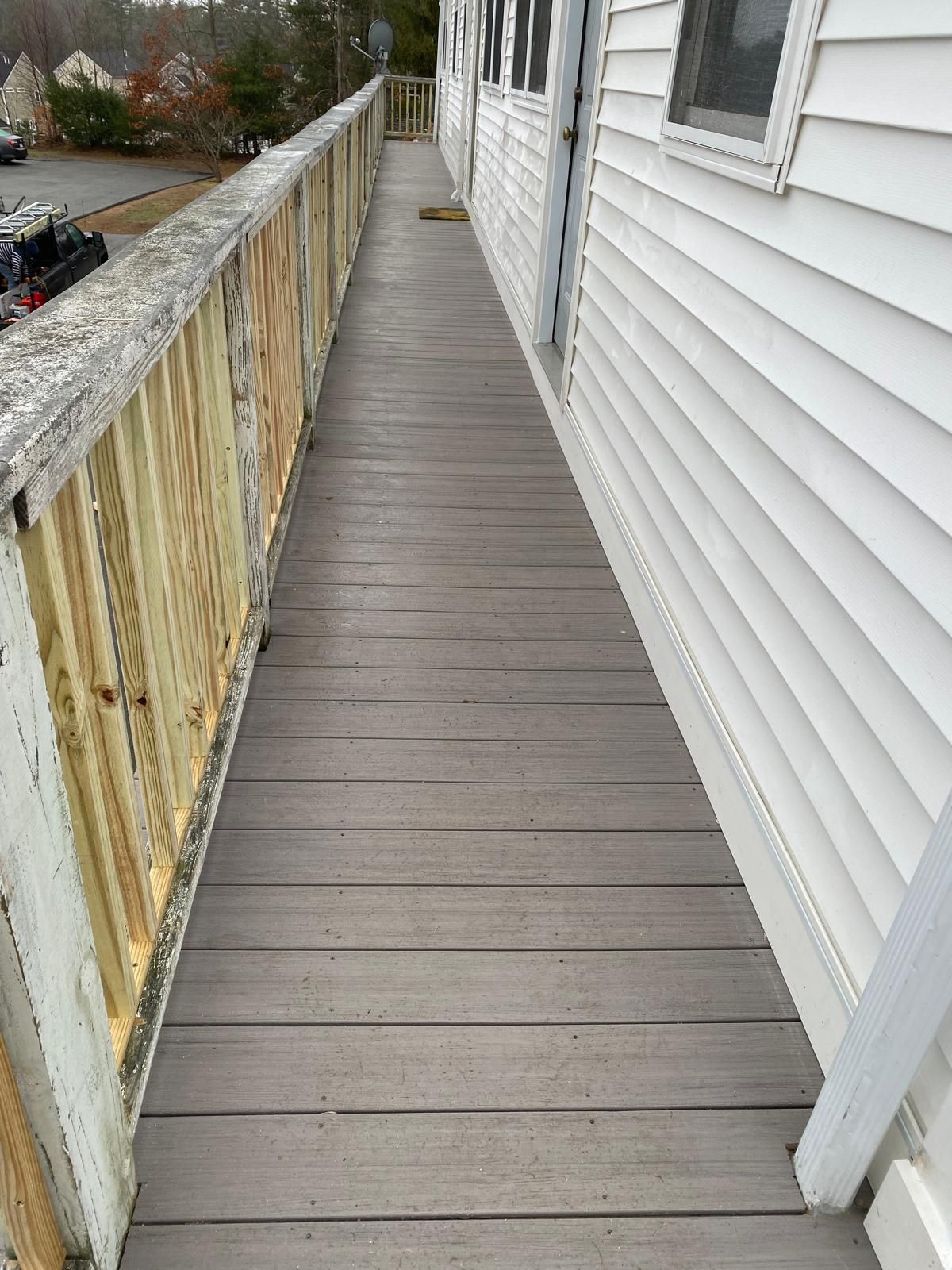 A narrow, weathered wooden walkway alongside a white-sided building with windows and a railing.