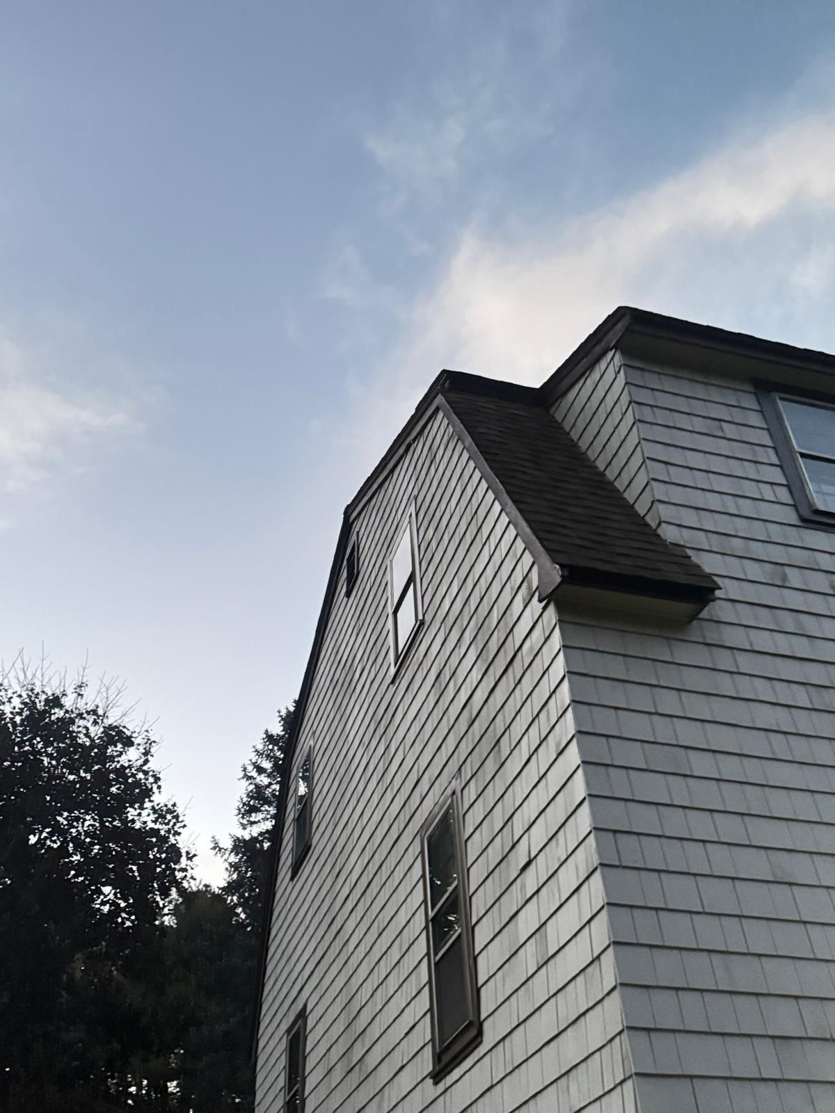 Side view of a white shingle-sided building with a dark roof and windows against a blue sky.