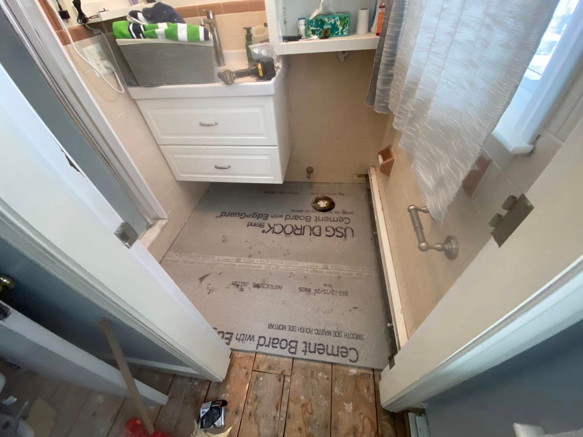 Bathroom remodel: Cement board floor, vanity, shower area, and open doorway with exposed wood flooring.